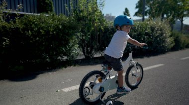 Aktif küçük çocuk dışarıda bisiklet sürüyor yeşil yolda kask takıyor.