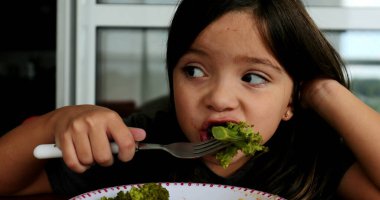 Öğle yemeğinde brokoli yiyen küçük kız sağlıklı sebze yiyor.