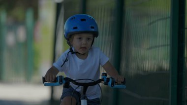 Dışarıda bisiklet süren aktif bir çocuk. Kasklı küçük bir çocuk bisiklet sürüyor.