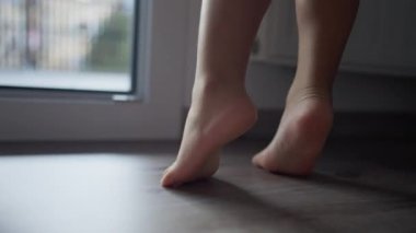 Child feet closeup on tiptoes at home. Little kid walking barefoot indoors