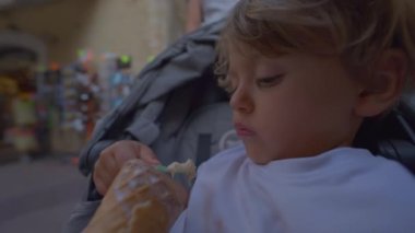 Child eating ice cream cone seated in stroller. One small boy eats sweet dessert enjoying vacations