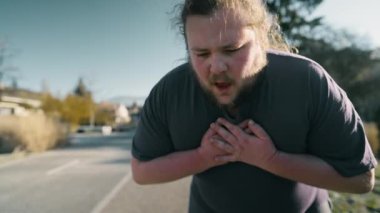 Person suffering from physical pain outdoors. Man unable to breath with hands on chest gasping for air having heart palpitations