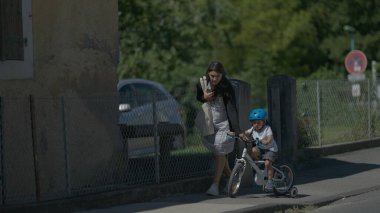 Child riding bicycle outside at park with mother