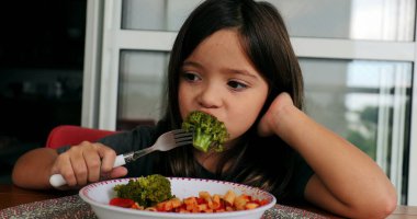 Brokoli yiyen küçük kız öğle yemeğinde sağlıklı sebze yiyor.