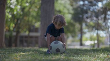 Küçük çocuk dışarıda futbol topunu tekmeliyor.