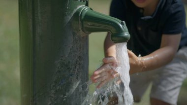 Küçük çocuk musluk suyu kullanarak dışarıda ellerini yıkıyor.