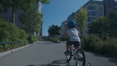 Çocuk dışarıda bisiklet sürüyor, koruyucu başlık takıyor.