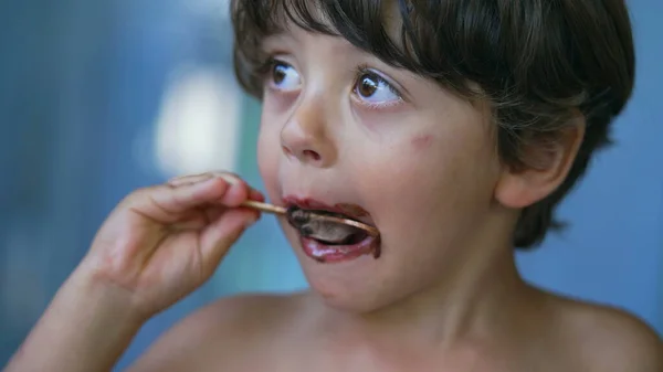 Closeup child face finishing icecream dessert. Messy young boy mouth covered in chocolate enjoying ice cream