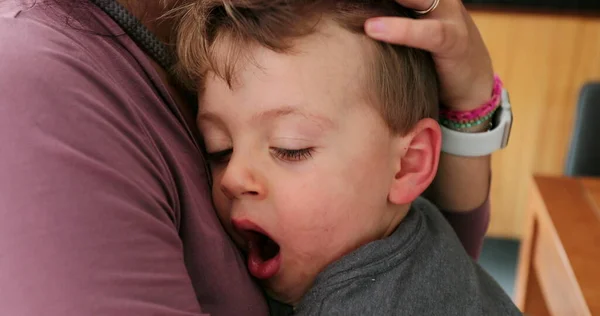 Sleepy child yawning on mother lap mom caressing tired toddler
