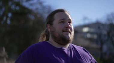 One pensive happy young man walking forward outside smiling. A joyful overweight guy walks outdoors feeling positive. Tracking shot