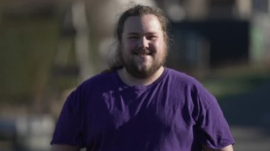 One happy chubby man smiling at camera standing outside. Closeup face of an overweight joyful casual person. Tracking shot