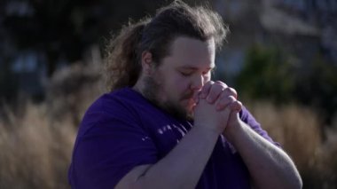 One Spiritual young man raising arms in the air asking for God help. Dramatic person praying with hands clenched feeling grateful. Hope and Gratitude concept