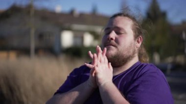 One young man praying to God during hard times. Faithful person in prayer outdoors clenched hands together seeking help