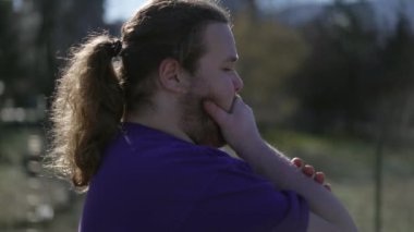 Concerned young man standing outdoors feeling anxiety. Closeup face tracking shot on overweight male person with preoccupied expression