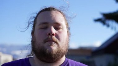 Serene calm millennial young man with eyes closed in meditation outdoors. A fat overweight person having peace of mind in contemplation