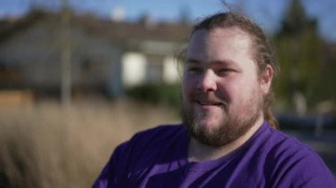 Young man standing outside smiling feeling pleased. One casual happy positive overweight male person. Tracking shot