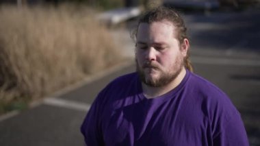 One worried overweight man standing outside with preoccupied expression. A thoughtful fat guy close up face with anxious emotion. Tracking shot