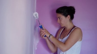 Woman painting home corners with paint roller. Woman doing house renovation painting purple wall with white color. DIY