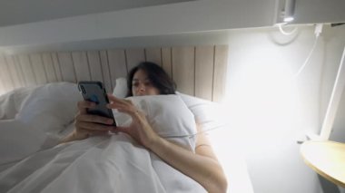 Woman shutting off cellphone and lamplight going to bed. Person turning light off