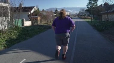 Back of one overweight man running outside in street. A fat person getting back into shape. Motivational concept