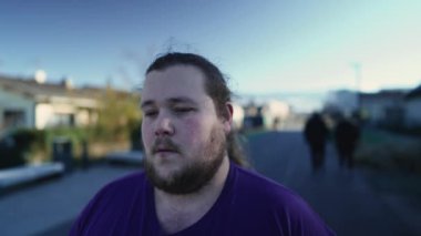 One pensive overweight young man walking outside in street in contemplation. A meditative young fat male person. Tracking shot