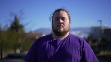 One calm man meditating outside. A chubby guy portrait with eyes closed relaxing outdoors in contemplation. Tracking shot