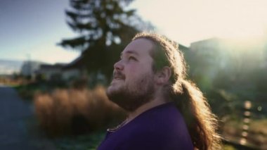 One joyful overweight young man standing outdoors looking at sky with HOPE. Closeup face of contemplative male person