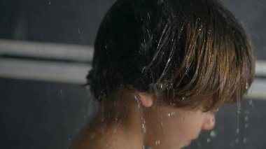Küçük tatlı bir çocuk yavaş çekimde duşa giriyor. Duş alan çocuk saçlarından damlacıklar dökülen yakın çekim yüzü