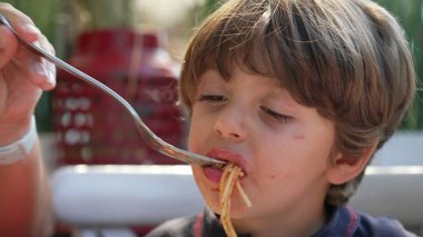 Anne öğle yemeğinde çocuk spagettisini besliyor. Kırmızı soslu makarna yiyen küçük bir çocuk. Yaşam tarzı aile yemeği.