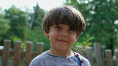 Parkta kameraya gülümseyen bir çocuk.