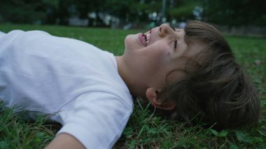 Mutlu bir çocuk çimlere uzanmış gülümsüyor ve gülüyordu. Parkta yatan erkek çocuğun yüzünü kapat.