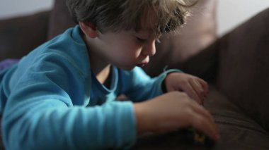 Küçük bir çocuk kanepeye uzanıp oyuncaklarla oynuyor. Çocuk evdeki kanepede pijamalarıyla oynuyor.