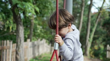 Küçük çocuk oyun sahasında ipe uzanıyor. Açık havada oynayan aktif bir çocuk