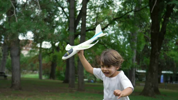 One happy child running outside with plane glider toy. Kid throwing airplane at park
