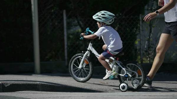 Child cyclist crossing street with mother in street. Parent helping kid at crosswalk. Boy wearing helmet on wheels
