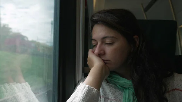 Woman sleeping by train window with hand in chin asleep. Female passenger napping while commuting to work or study by high speed transportation