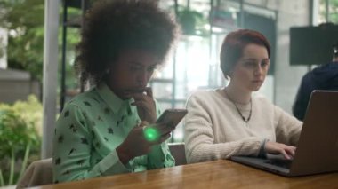 Young people using modern technology at coffee shop. Two women looking at laptop and phone screen