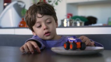 One small boy seated at table with car toy. Child wearing pajama in the morning holding toy vehicle