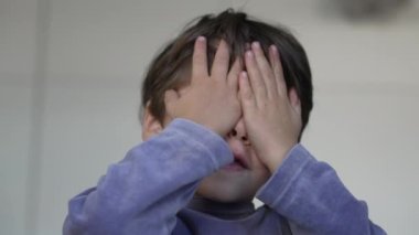 Shy child covering eyes with hands. Close up cute small boy hiding face