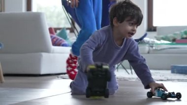 Child playing with firetruck toy car on floor. Little boy wearing pajama plays with toys indoors during Christmas day