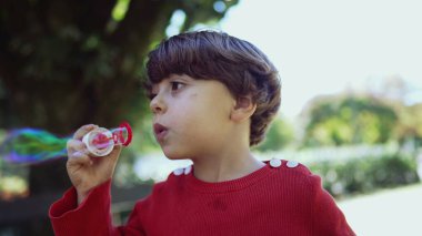 Parkta baloncuk çıkaran sevimli mutlu çocuk. Küçük bir çocuk dışarıda gülümsüyor.