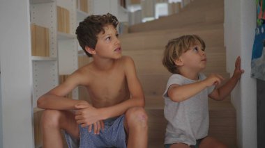 Evde merdivenlerde oturan iki genç kardeş. Kardeşler bir arada. Samimi, özgün aile anı. Büyük kardeş küçük çocukla takılıyor.