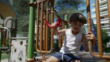 Oyun parkındaki maymun barına tutunan küçük bir çocuk. Aktif çocuk güneşli bir günde dışarıda egzersiz yapıyor.