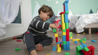 Çocuk zemindeki yapı taşlarıyla oynuyor. Çocuğun kazara kuleyi yıkarken çekilmiş bir fotoğrafı. Yatak odasında oynayan küçük bir çocuk.