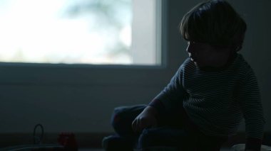 Karanlıkta oturan bunalımlı bir çocuk. Yalnız küçük çocuk pencerenin yanında yerde yatıyor. Hüzünlü zorba çocuğun silueti