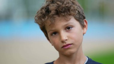 Düşünceli bir ifadeyle kameraya bakan ciddi bir çocuğun portresi. Üzgün, düşünceli bir erkek çocuk dışarıda bekliyor.