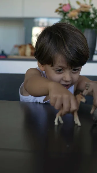 Child playing with toys at home. One small boy plays with toy horses plays on table in Vertical Video