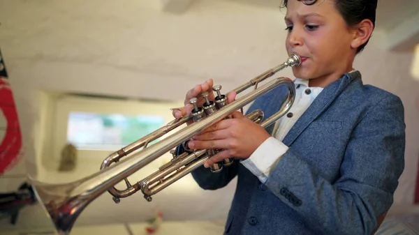 Young boy playing trumpet indoors. Teen child practicing musical instrument