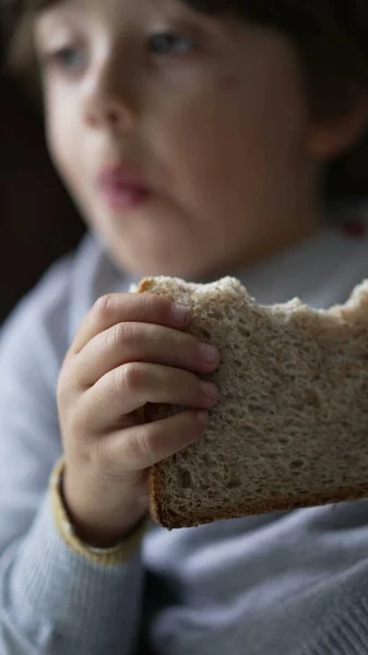 Child eating sandwich. Closeup small boy hand holding carb food snack. Kid laying on couch in Vertical Video