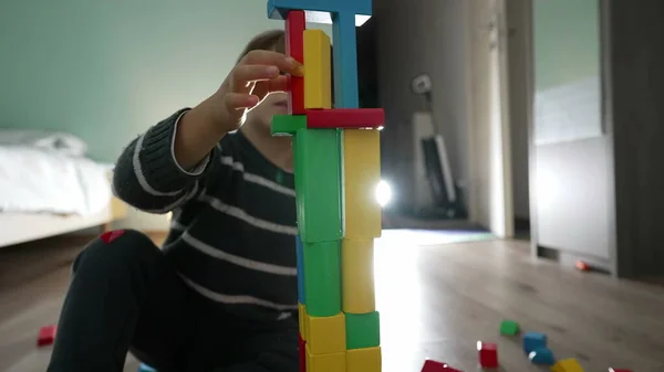Small boy plays with building blocks. Child dropping block accidentally. Kid making tower in bedroom play